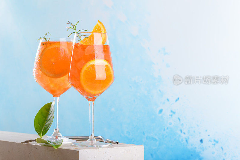 经典的意大利开胃酒aperol spritz鸡尾酒在两个杯子与冰，橙色的蓝色背景，大理石平台